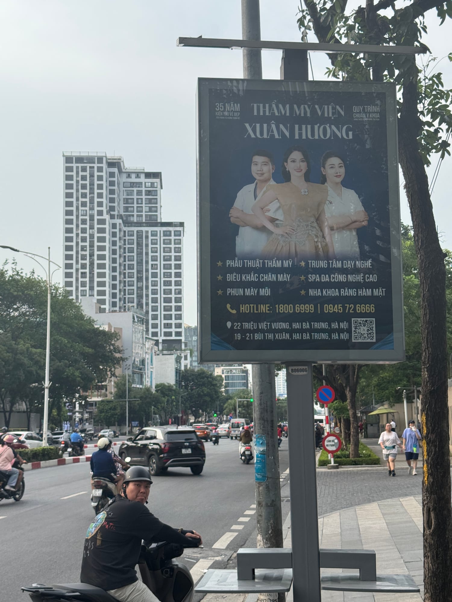 Poster tại giao lộ đông người, phía sau là tòa nhà cao tầng
